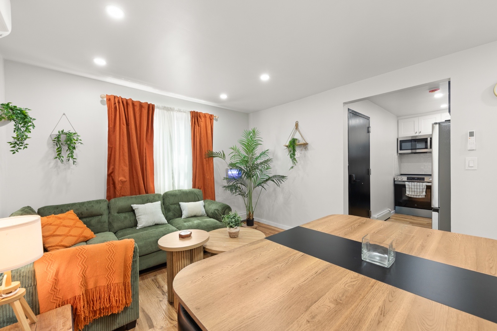 Shared living room with green corduroy sofa, orange curtains and dining table